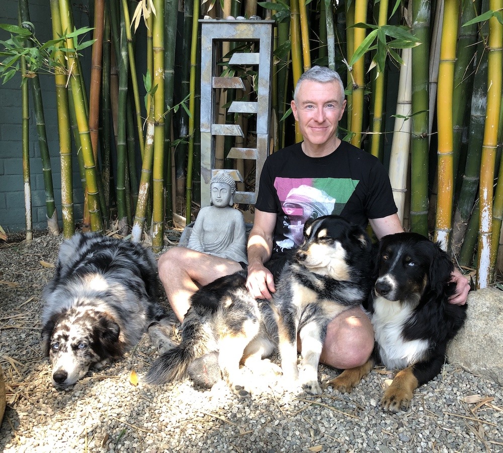 Michael R. Burke animal communicator sitting with three dogs in a bamboo garden