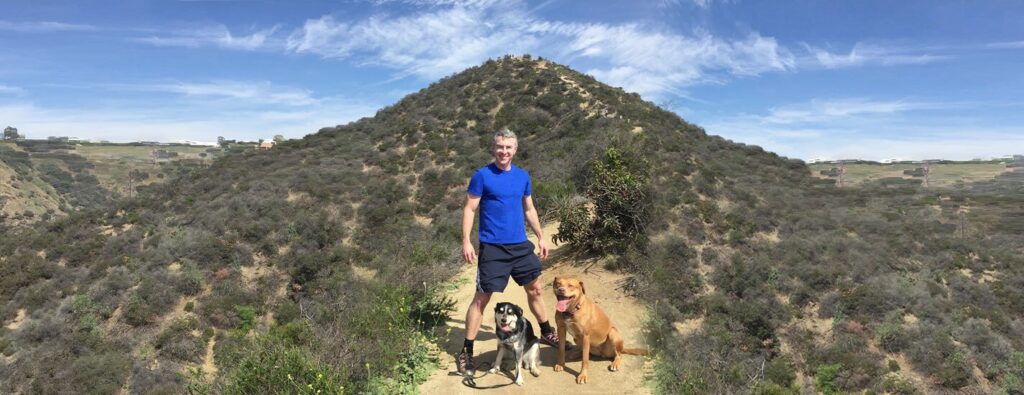 Man Hiking with Dogs on a Hillside Trail