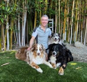 A man sits on grass with three happy dogs in a bamboo garden, showcasing a serene, pet-friendly environment.