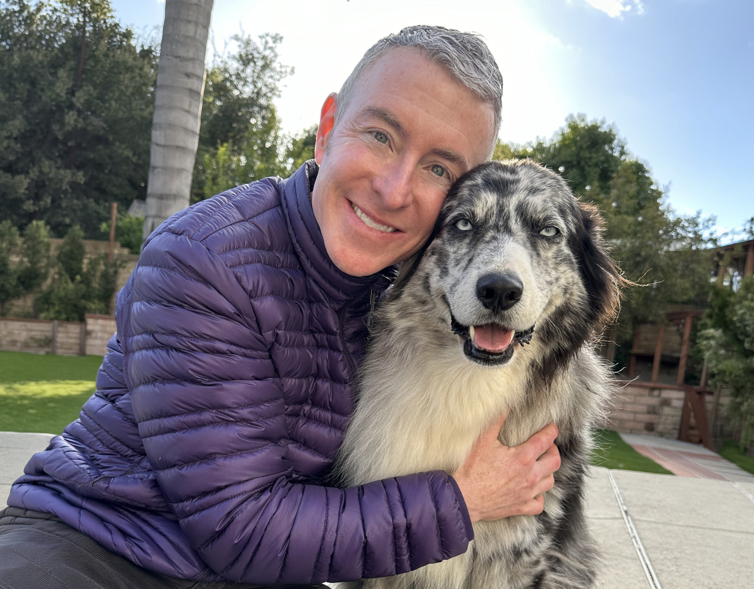 Man Hugging a Large Fluffy Dog While Smiling