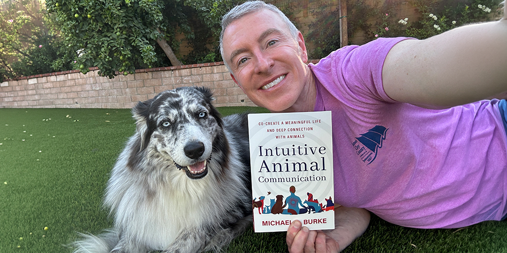 Michael R Burke relaxing with his dog whilst holding his animal communication book